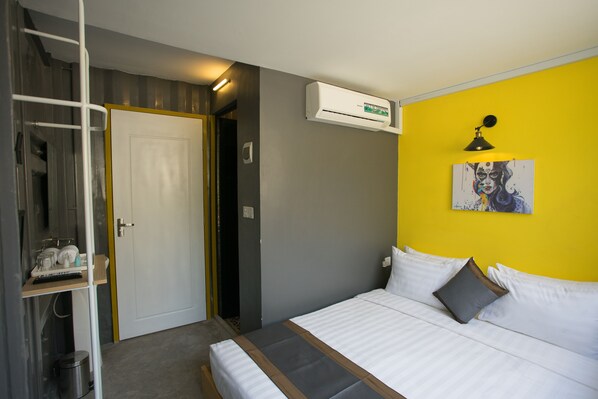 A bedroom with a bed, a white door, a shelf with toiletries, an air conditioning unit, and a painting on the wall. - White Rabbit Hostel - Adults Only (Siem Reap)