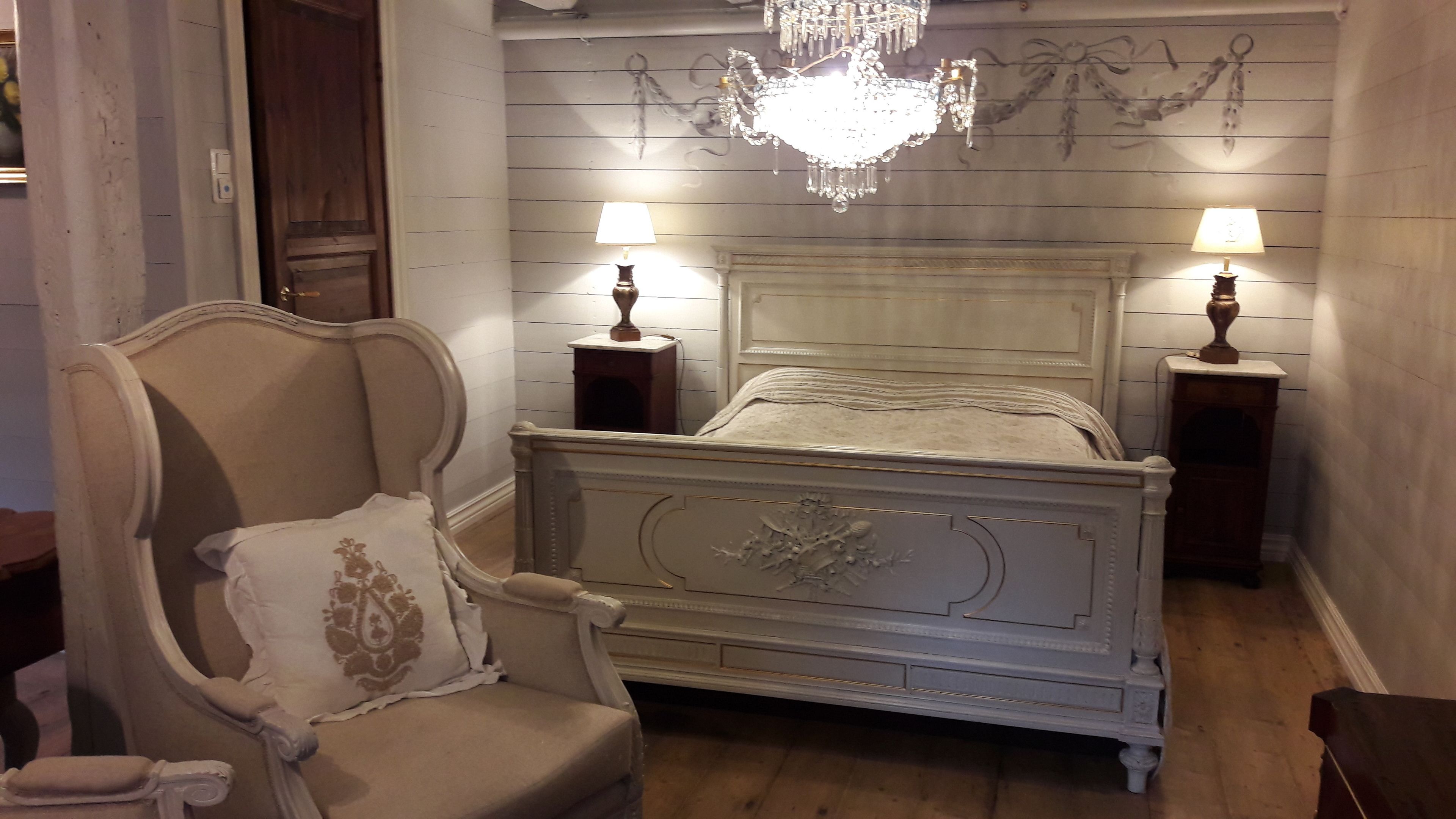 A bedroom with a classic bed, two bedside lamps, a chandelier, and a wooden wall paneling.