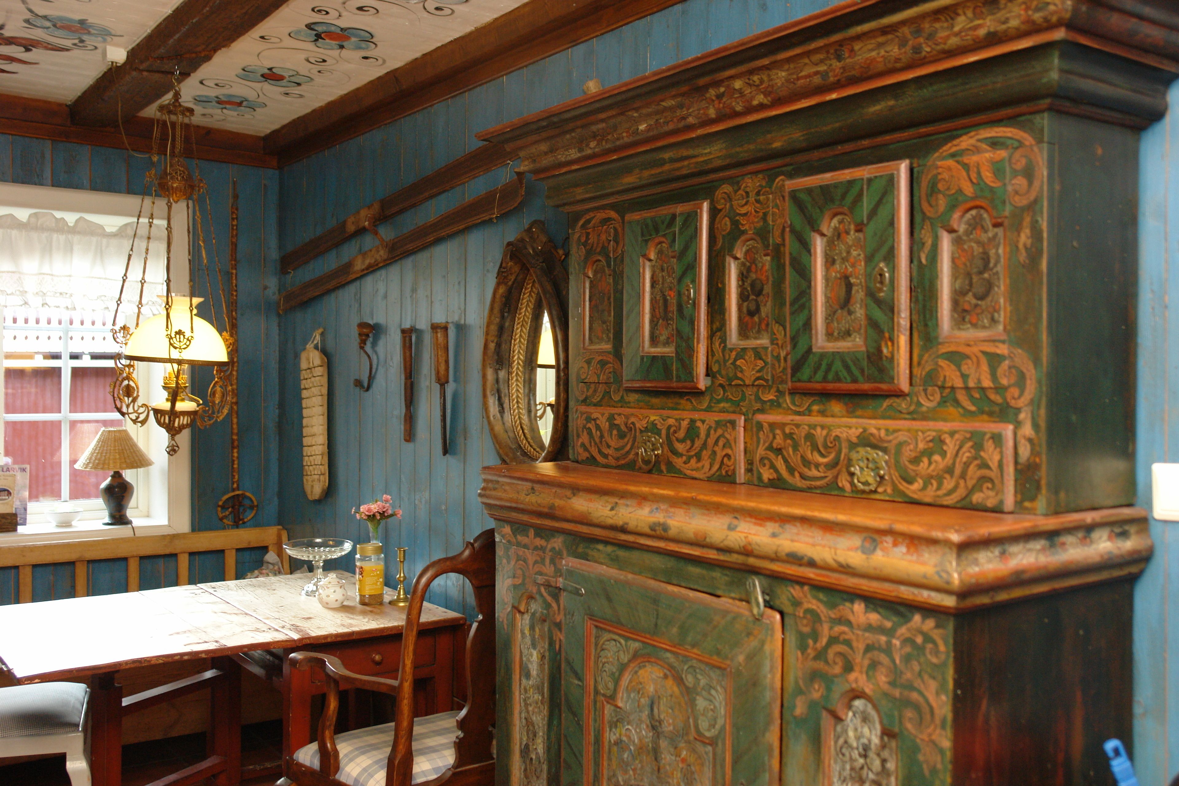 A room with a wooden dining table, chairs, a chandelier, and a decorative cabinet with intricate designs.
