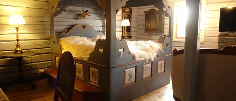 A four-poster bed with a decorative headboard, a bedside table with a lamp, and a dresser with a mirror.