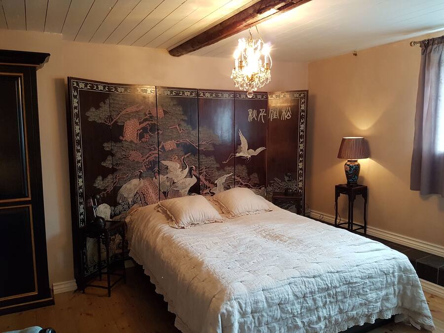 Un dormitorio japonés tradicional con una cama grande, una puerta corredera decorativa con motivos naturales, una araña y una mesita de noche con una lámpara.