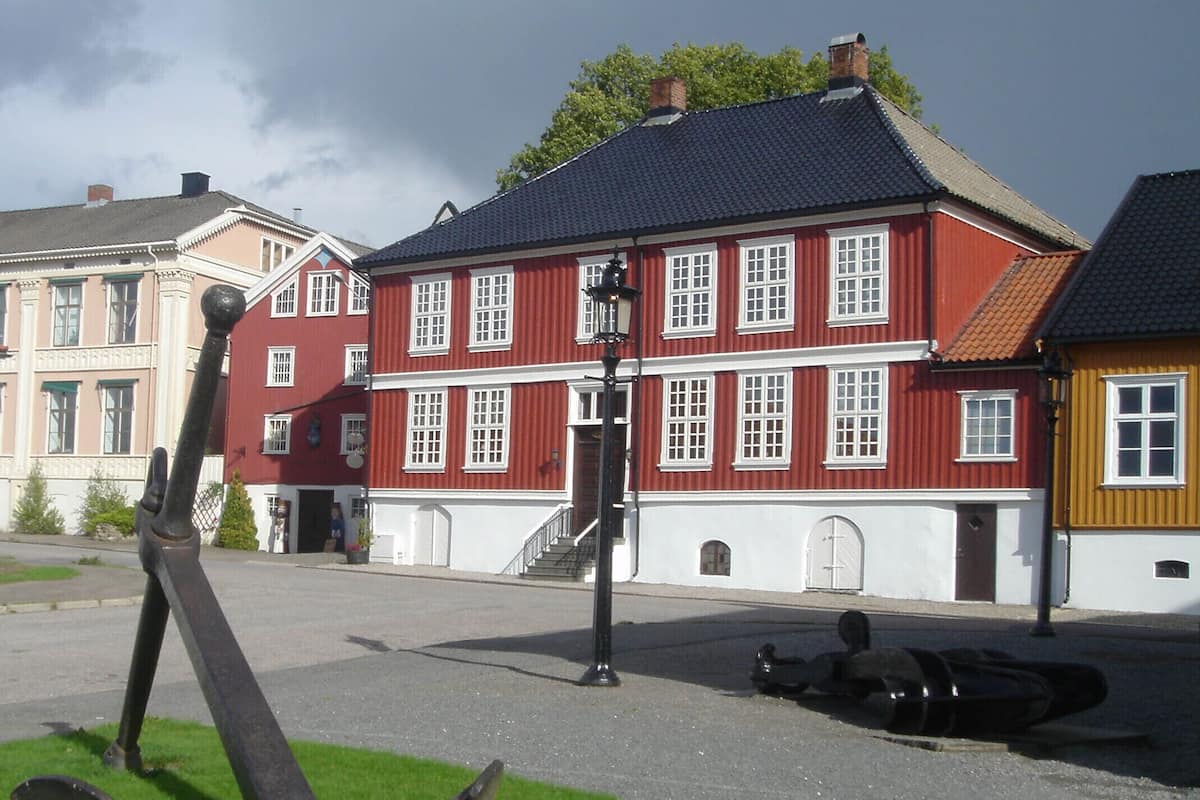 A red building with white trim and multiple windows, a street lamp, and a grassy area with an anchor sculpture.