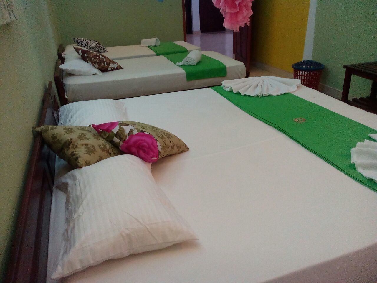 A hotel room with two single beds, each with a green bedspread and white pillows.