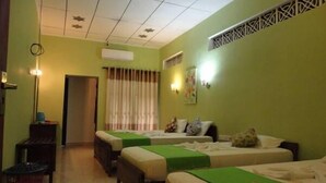 A hotel room with two beds, a desk, a chair, a trash bin, and a door. - Villa De Rosh (Negombo)