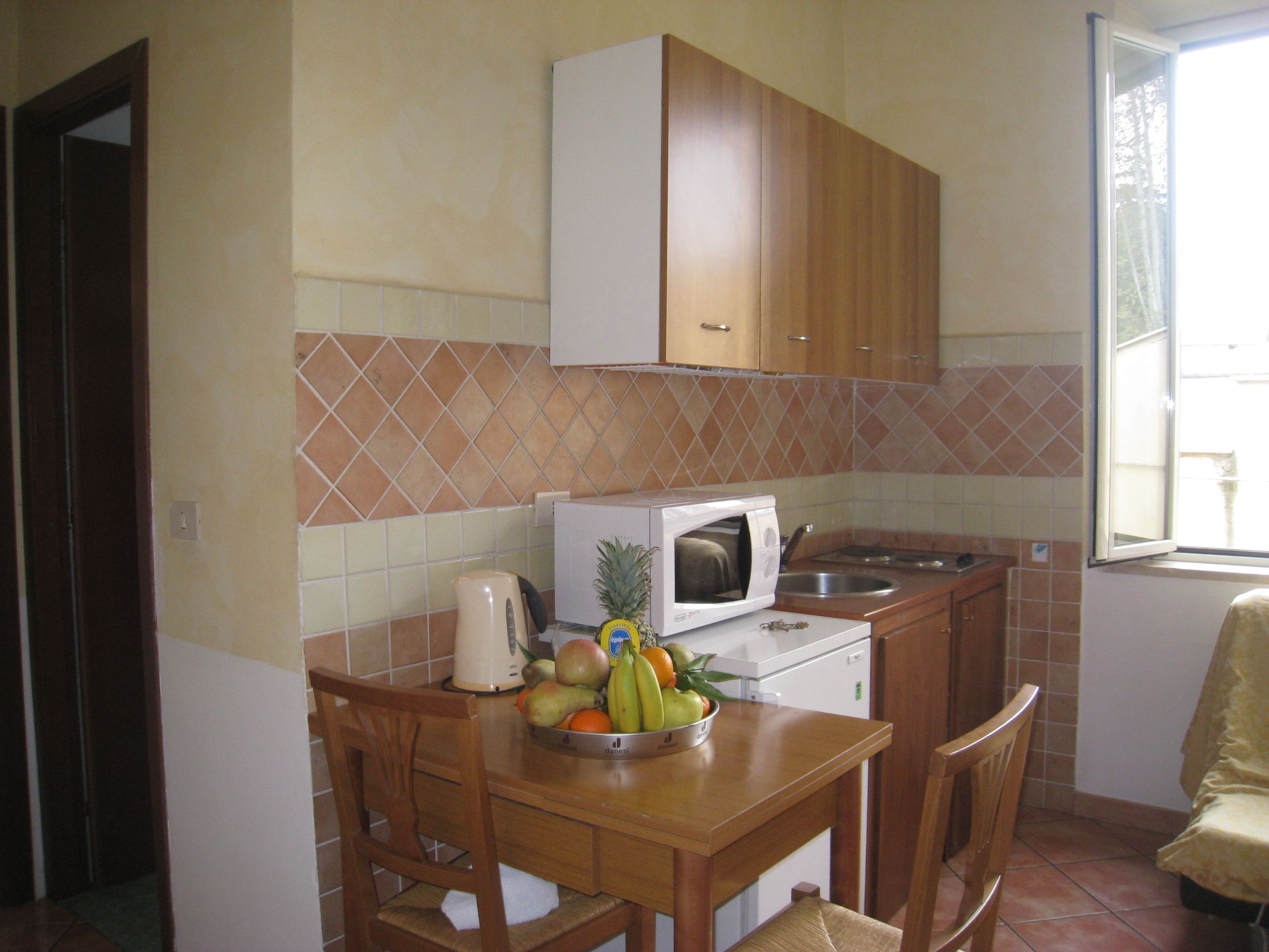 A compact kitchen with wooden cabinets, a microwave, a sink, and a fruit bowl on the counter.