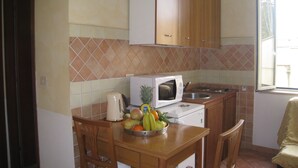 A compact kitchen with wooden cabinets, a microwave, a sink, and a fruit bowl on the counter. - Residenza Camilla (Rome)