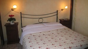 A bed with a floral bedspread, two bedside tables with lamps, and a wall-mounted light fixture. - Residenza Camilla (Rome)