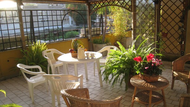 A covered patio area with wicker furniture, potted plants, and a table with a pitcher and cups. - Residenza Camilla (Rome)