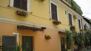 A yellow building with a tiled roof, numbered doors, and potted plants. - Residenza Camilla (Rome)