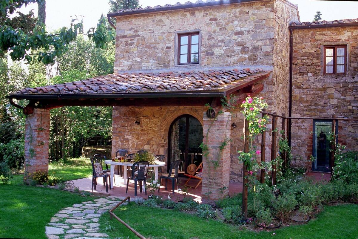 Un edificio de piedra con un patio, mobiliario exterior y un jardín.