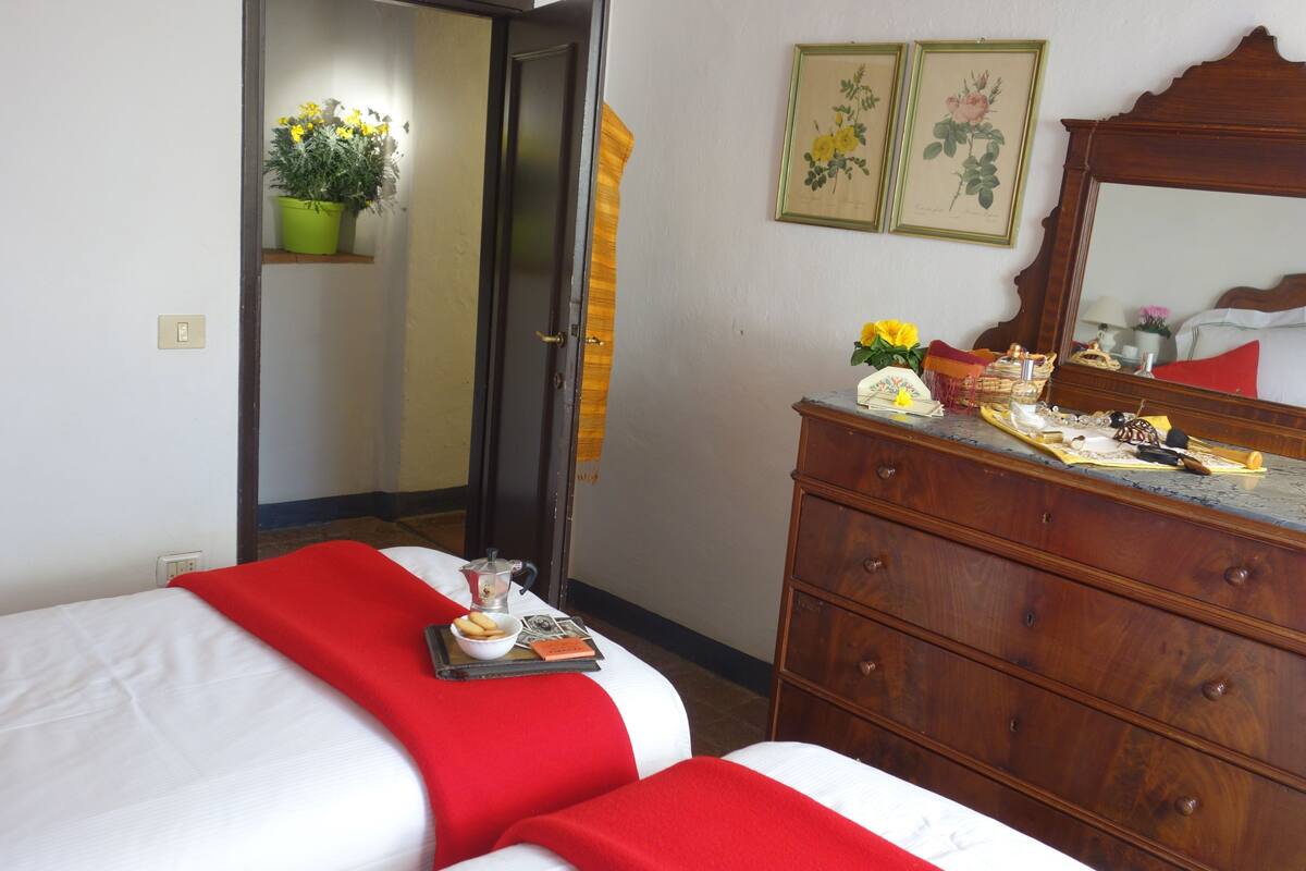 Habitación de hotel con dos camas, un aparador de madera, un espejo y una puerta que da a otra habitación.