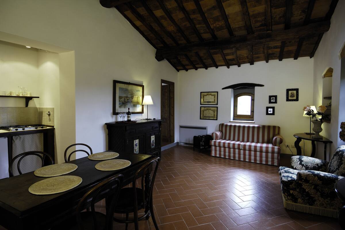 Un comedor con una mesa y sillas de madera, una cocina con estufa y una sala de estar con sofá y sillones.