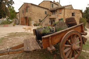 Un edificio rústico de piedra con un carro de madera y un perro en primer plano.