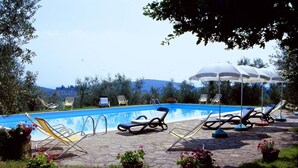 Una piscina con sillones de playa y sombrillas, rodeada de plantas en macetas y un sendero de piedra.
