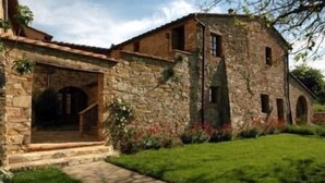 Un edificio de piedra con un portal central, un pequeño porche y un jardín cubierto de césped.
