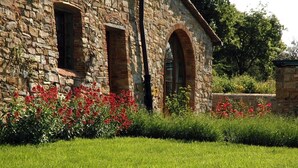 Un edificio de piedra con ventanas arqueadas y un jardín cuidado con flores rojas.