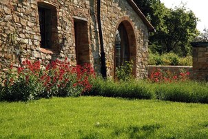 Un edificio de piedra con ventanas arqueadas y un jardín cuidado con flores rojas.