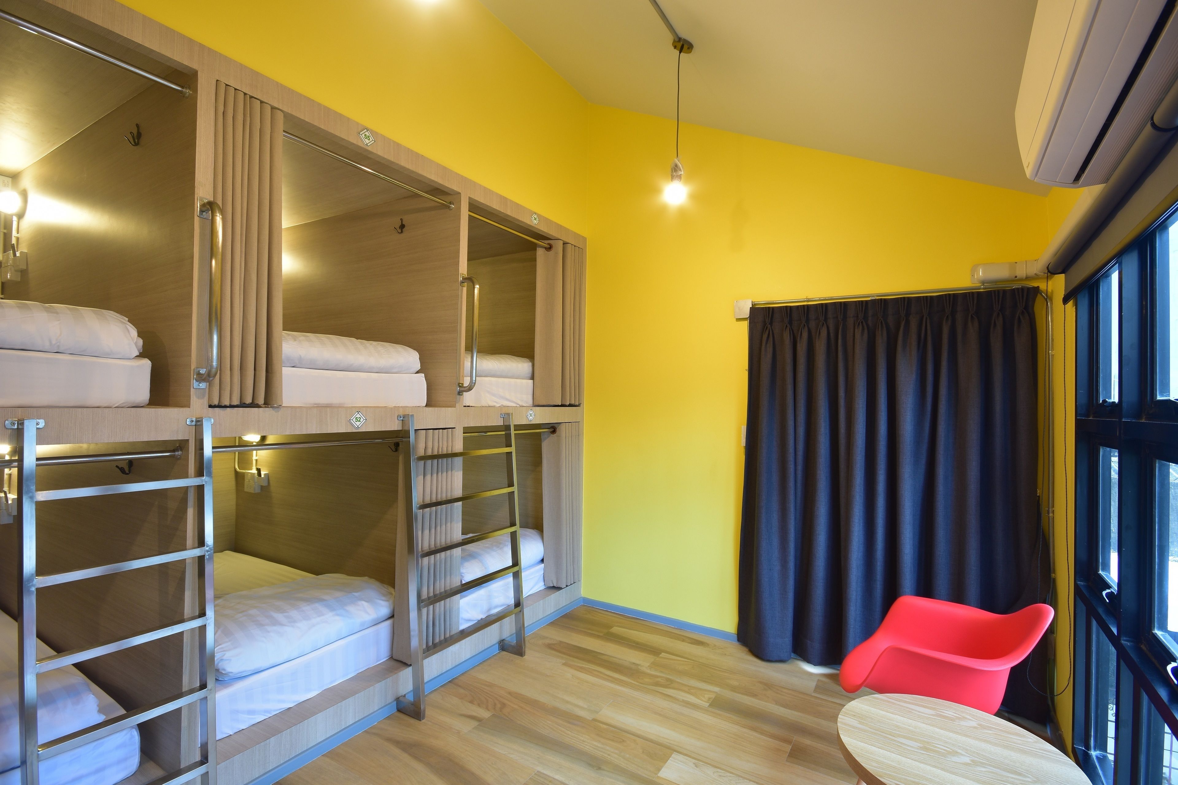 A room with bunk beds, a red chair, and a large window with curtains.