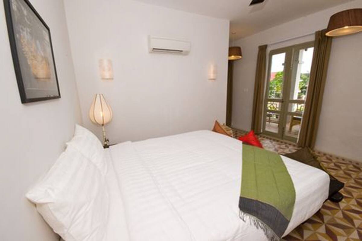 Habitación de hotel con cama, aire acondicionado de pared, ventana con cortinas y vista al exterior.
