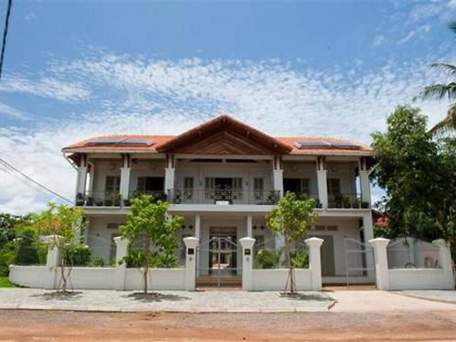A two-story house with a red-tiled roof, a balcony on the upper floor, and a gated entrance.