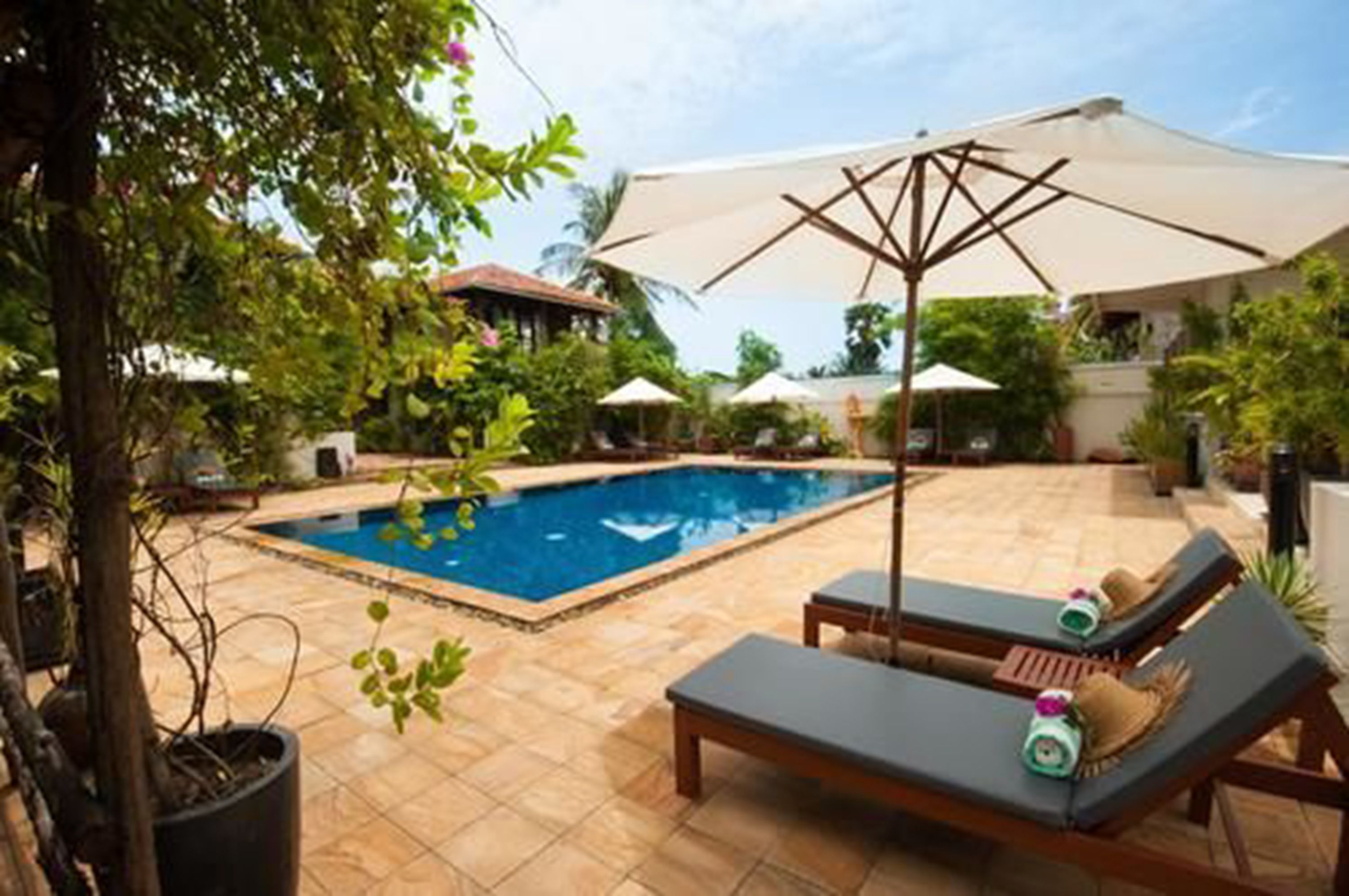 A swimming pool with lounge chairs and umbrellas, surrounded by greenery and a tiled patio.