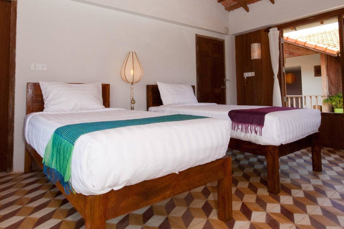 Una habitación con dos camas de madera, una lámpara y un suelo a cuadros.