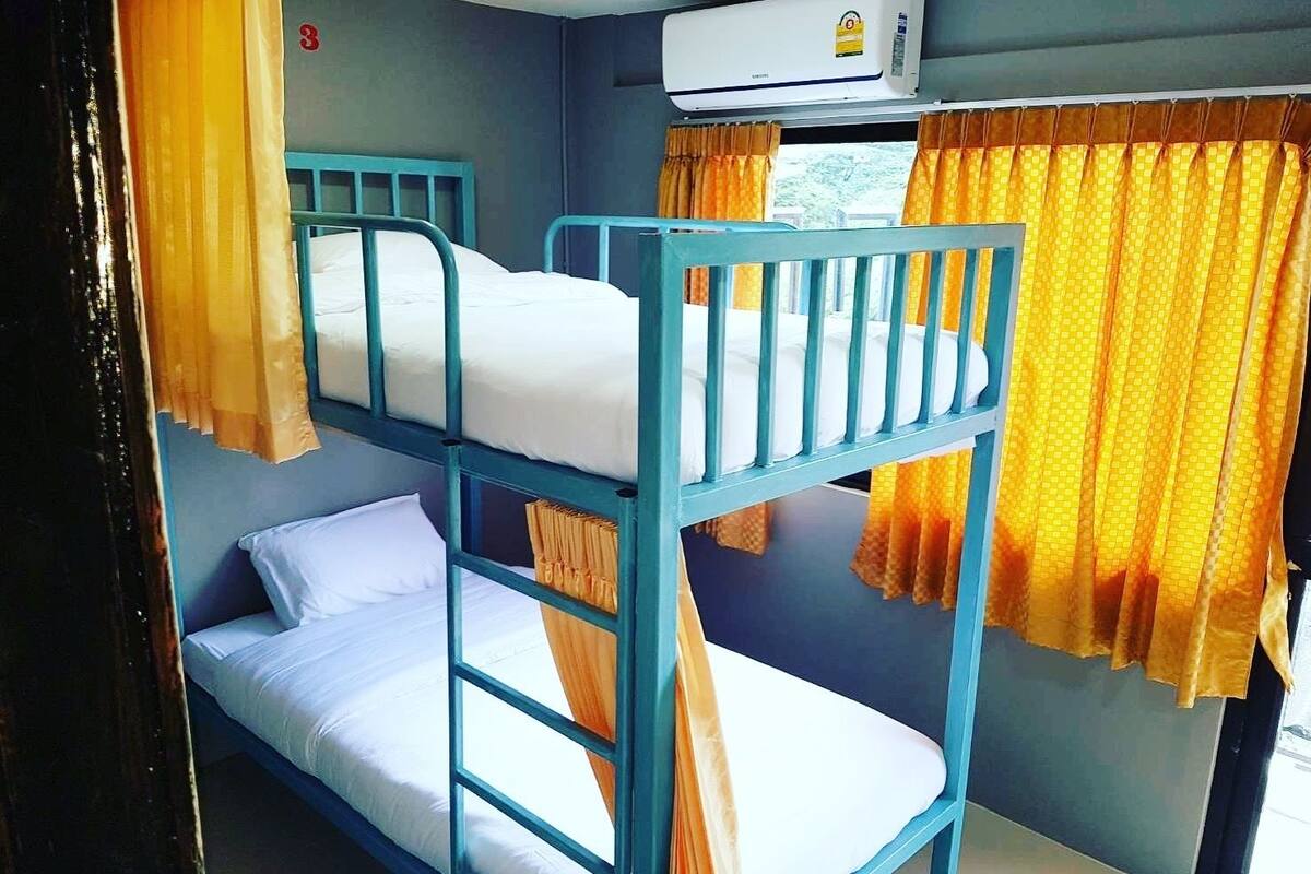 A bunk bed room with a window, curtains, and an air conditioning unit.