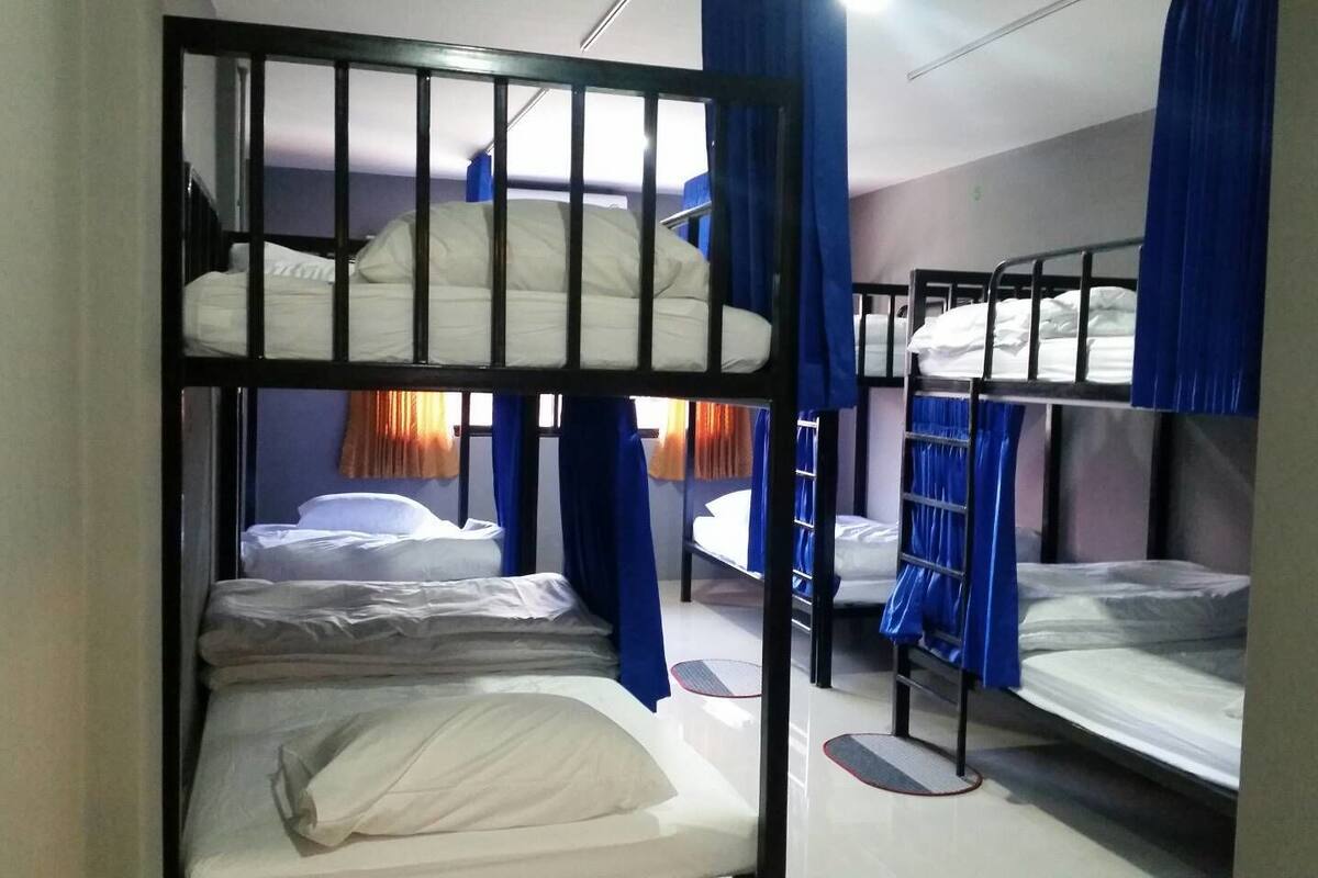 A dormitory room with bunk beds, blue curtains, and a window with orange curtains.