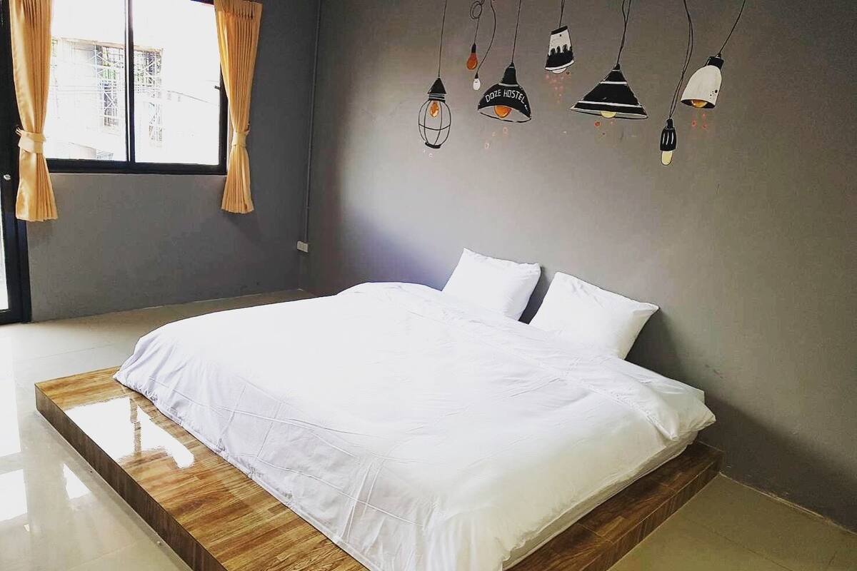 A modern bedroom with a large bed, a wooden platform, and a view of a construction site through the window.