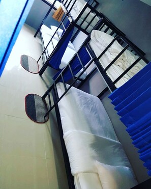 A dormitory-style room with bunk beds, a small table, and a window with blue curtains. - Doze Hostel (Chiang Mai)