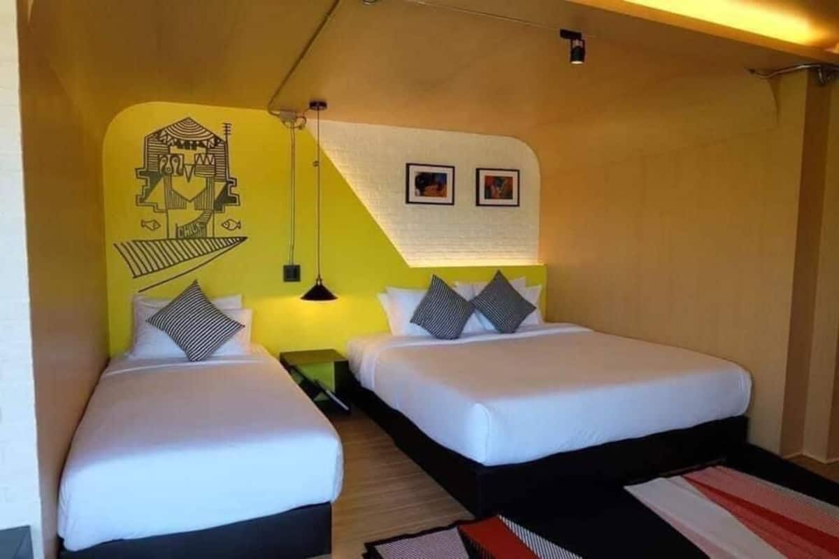 A room with two beds, a yellow accent wall, a black and white striped rug, and a hanging light fixture.