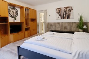 Een hotelkamer met een bed, een televisie, houten kasten, een klok en een wanddecoratie van olifanten.
