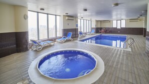 Una piscina interior con sillas de descanso y vista a la ciudad.