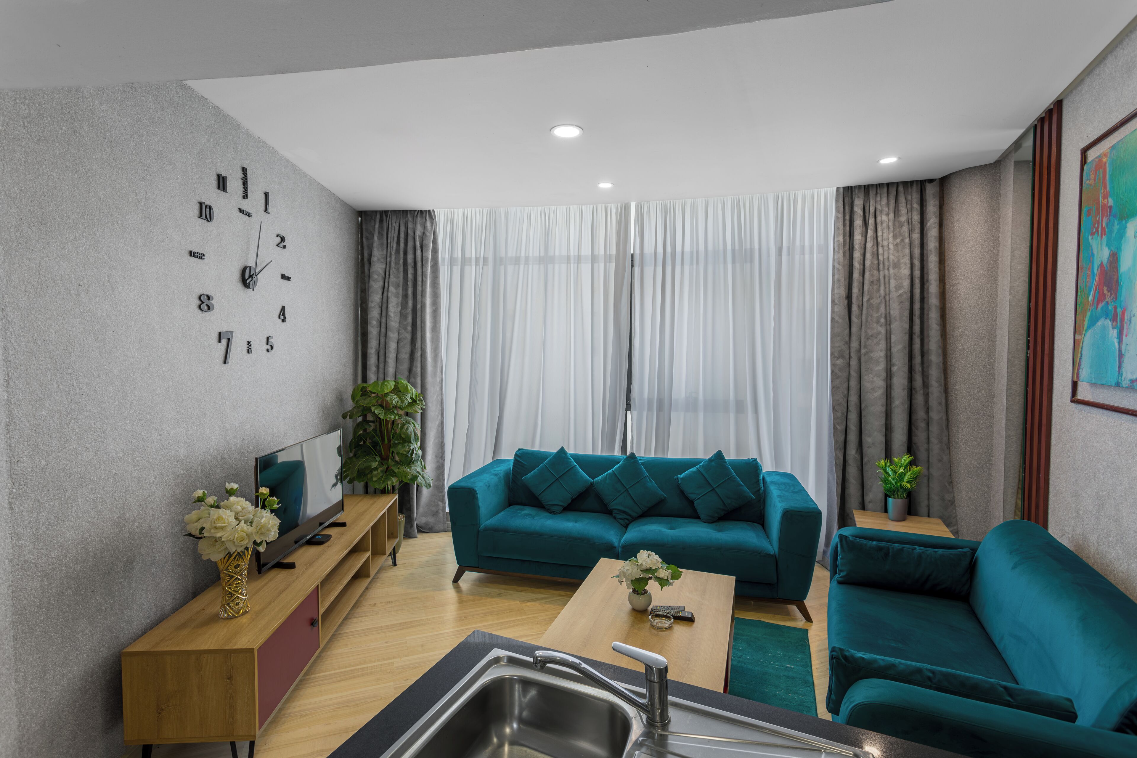 A modern living room with a teal sofa, a wooden coffee table, a TV on a wooden stand, and a wall clock.