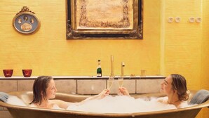 A bathtub with two people toasting with champagne, a framed picture on the wall, and a vintage clock.