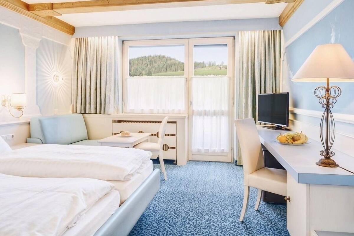 Hotellihuone, jossa on kaksi sänkyä, työpöytä, tuoli, televisio ja ikkuna, jossa on verhot.