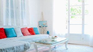 A bright living room with a white sofa, colorful cushions, a glass coffee table, and a view through a large window. - Klima Paradise (Samos)