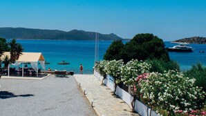 A coastal area with a clear blue sea, a paved walkway, and a small building with outdoor seating. - Klima Paradise (Samos)