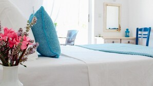 A bedroom with a bed, a white vase with pink flowers, and a blue pillow. - Klima Paradise (Samos)