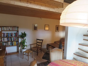 Una sala de estar acogedora con una estantería de madera, una mesa de comedor, un sillón cómodo, una planta en maceta y una escalera.