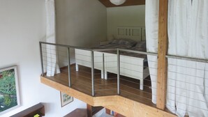 Ein Schlafzimmer mit einem Schlafpodest, einer Holzbalkendecke und einer Pendelleuchte.
