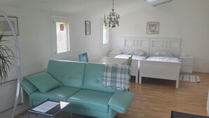 Ein modernes Wohnzimmer mit einem Türkis-farbenen Sofa, einem weißen Bett und einer Kristallleuchter.