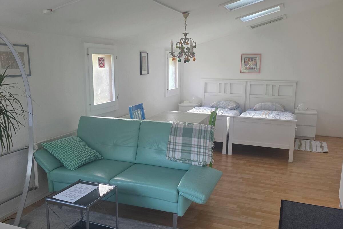 Una sala moderna con un sofá azul turquesa, una cama blanca y una araña.