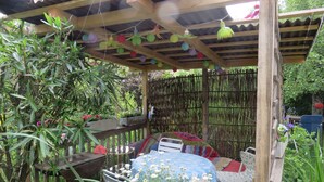 Ein überdachter Außenbereich mit Pergola, Holzmöbeln und verschiedenen Pflanzen.
