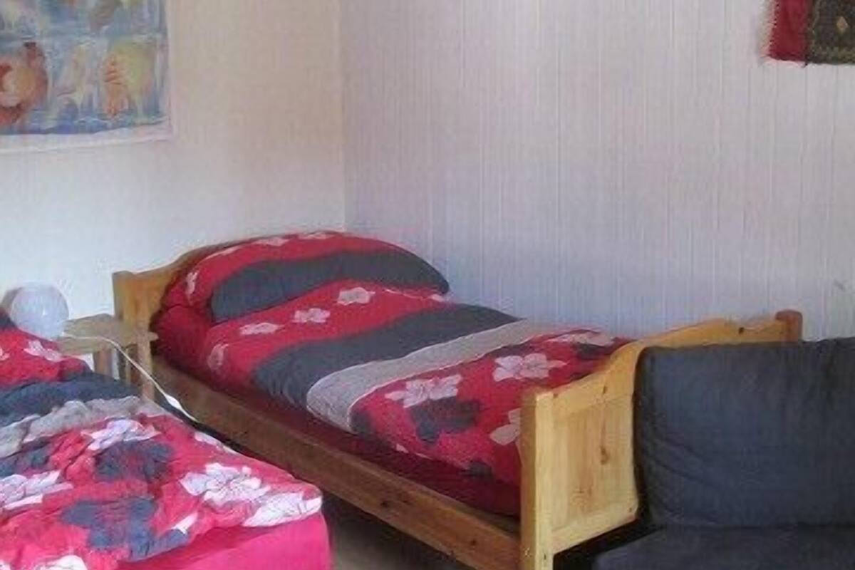 Una habitación pequeña y acogedora con dos camas individuales, un sofá gris y un cuadro en la pared.