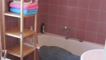 A bathroom with a wooden shelf holding towels, a bathtub, and a white sink.