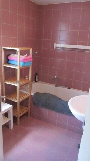 A bathroom with a wooden shelf holding towels, a bathtub, and a white sink. - Bed & Breakfast Erlach (Erlach)