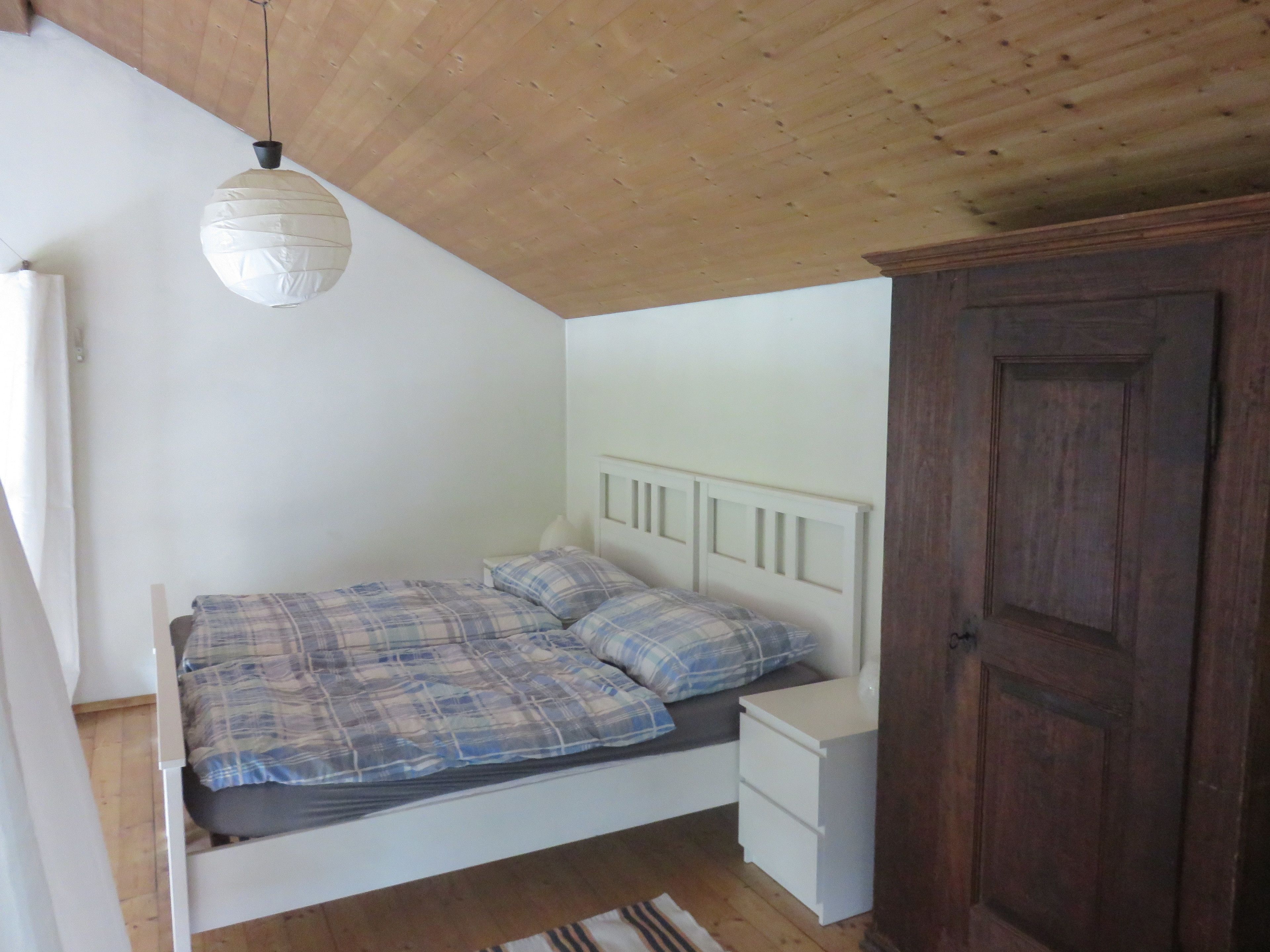 Une chambre à coucher comprenant un lit, des tables de chevet, une armoire en bois et un luminaire suspendu.
