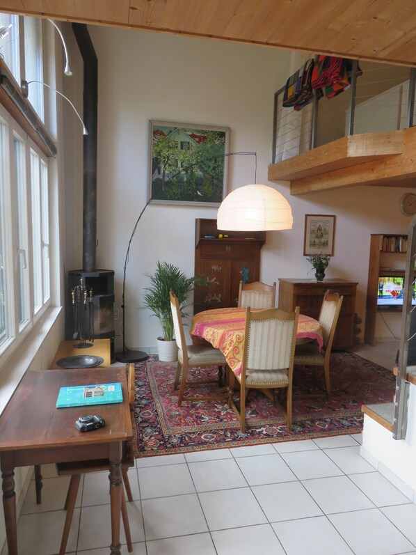 A cozy living room with a fireplace, wooden furniture, a dining table, and a large window. - Bed & Breakfast Erlach (Erlach)