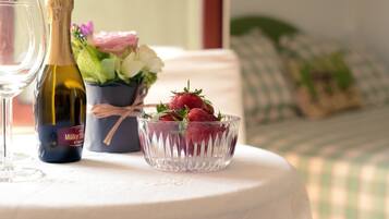 A table with a bottle of Müller Thurgau wine, a glass of wine, a bowl of strawberries, and a bouquet of flowers.